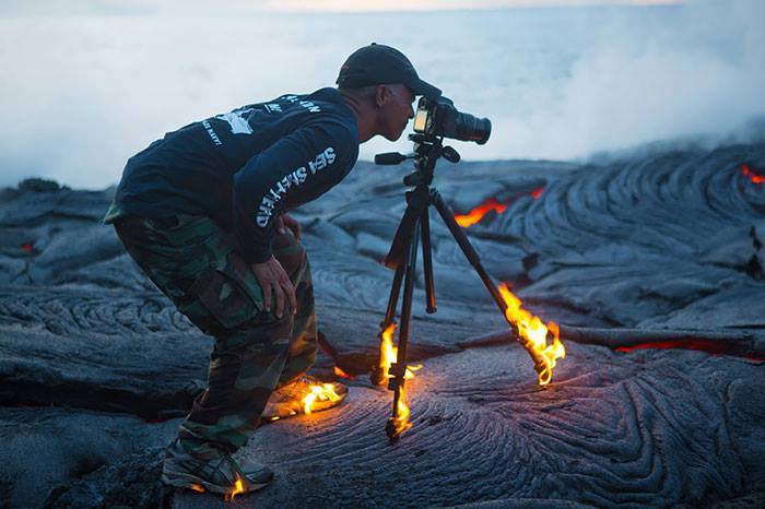 Photographer with tripod standing on burning lava, showing absolute disregard.