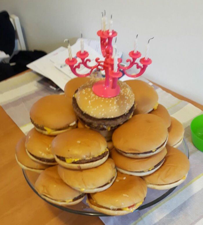 Hamburger cake stack topped with a pink candle holder, humorously styled like a birthday cake.