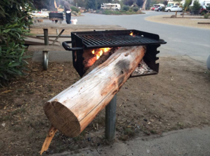 A large log awkwardly placed on a barbecue grill, partially burning.