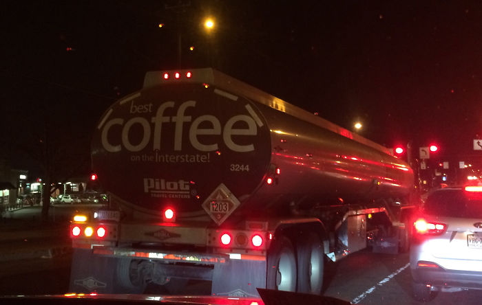 Tanker truck with "best coffee" on highway at night, reflecting lights.