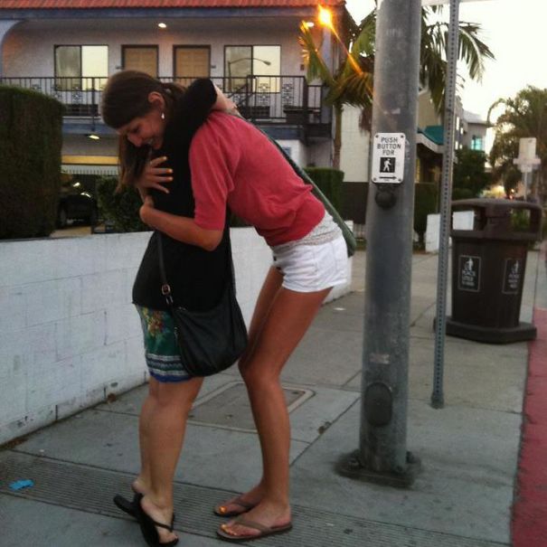 Tall people hugging shorter friend on sidewalk, highlighting everyday struggles of height difference in a casual urban setting.