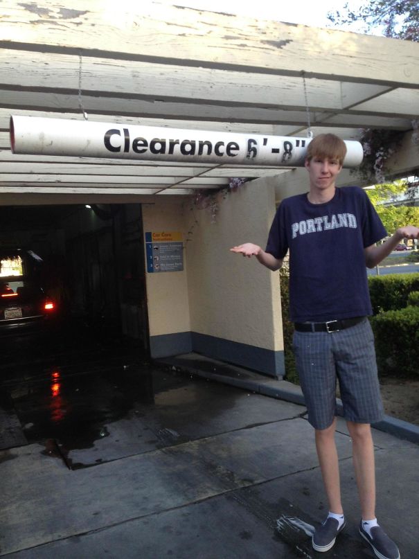 Tall person standing confused under a low clearance sign, illustrating everyday struggles of tall people in a parking garage.