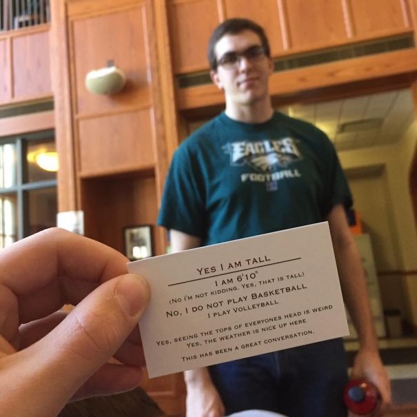 Tall person holding a card explaining common everyday struggles faced by tall people in a casual indoor setting.