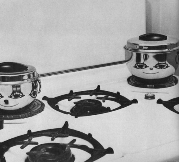Two shiny pots on a stove with reflective surfaces creating funny pareidolia faces on kitchen objects.