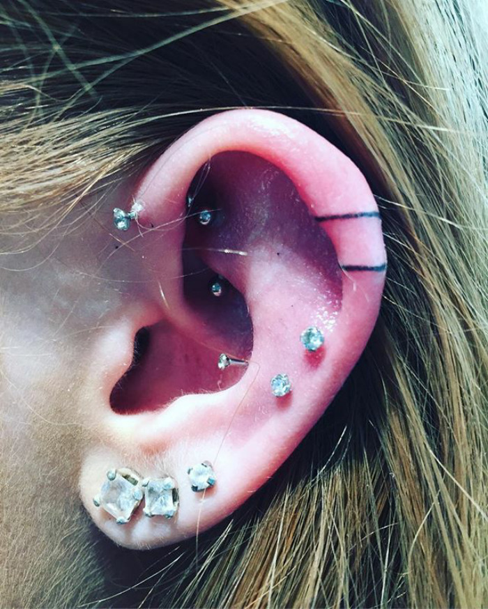 Close-up of an ear with a helix tattoo and multiple piercings, showcasing the Instagram helix tattoo trend.
