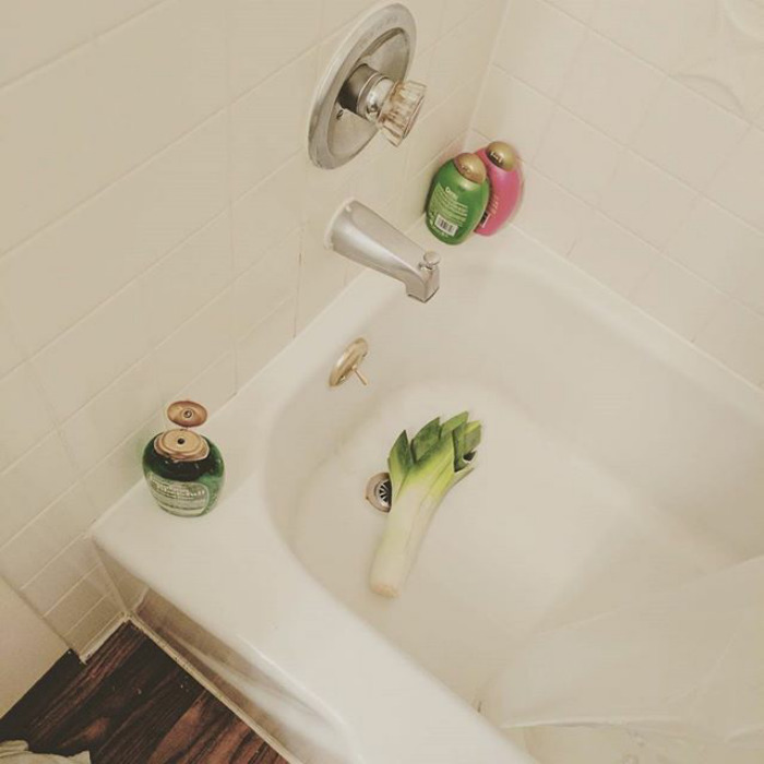 Leek in bathtub with shower products, showcasing a humorous touch wives might add.