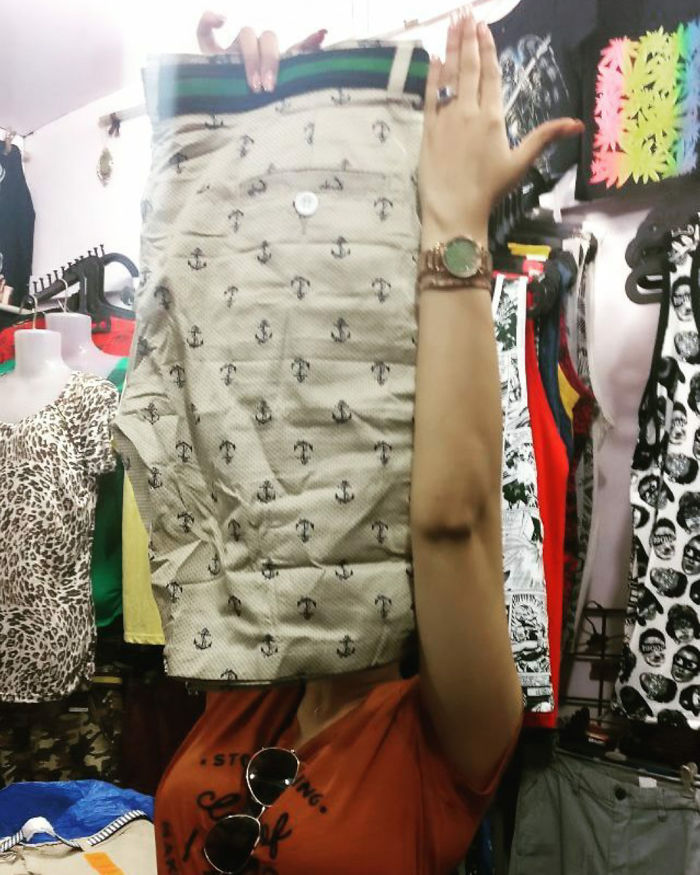 A woman humorously holds patterned shorts over her face in a clothing store.