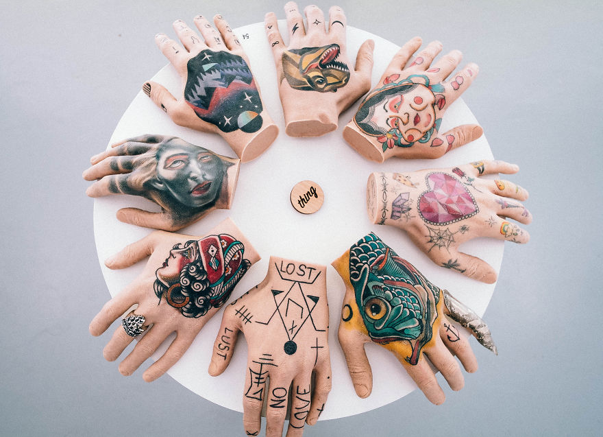 Tattooed mannequin hands arranged in a circle on a table; creative tattoo art display.