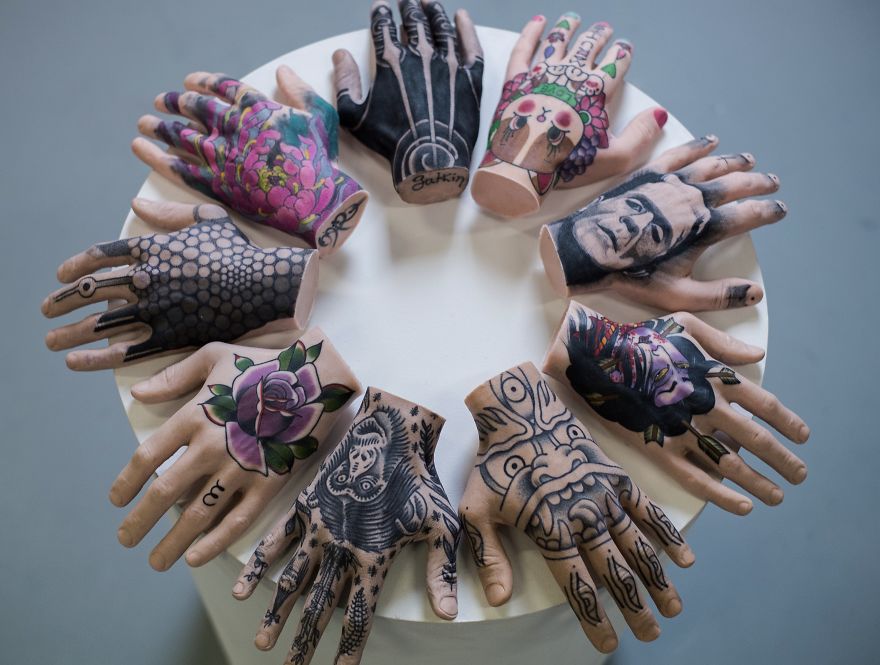 Tattooed mannequin hands arranged in a circle, showcasing various tattoo culture designs on a table.