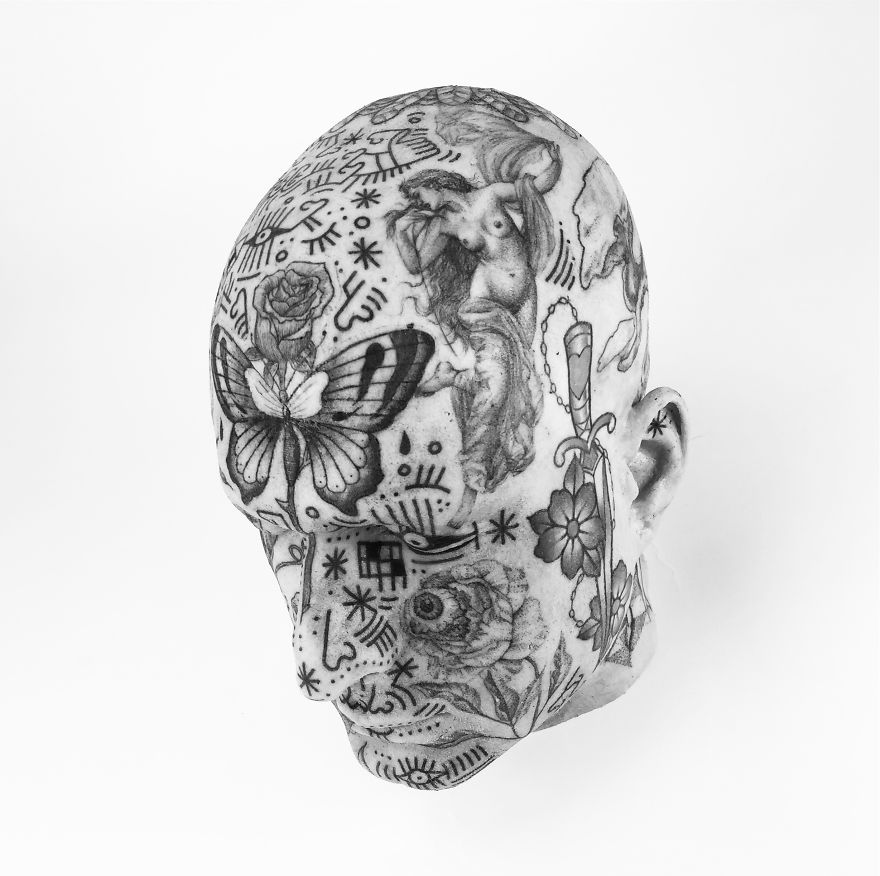 Tattoo culture writer's head covered in intricate black ink designs, featuring butterflies and abstract patterns.