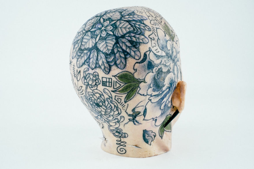 Tattoo culture writer showcases intricate head tattoo design on a mannequin head, illustrating creative energy.