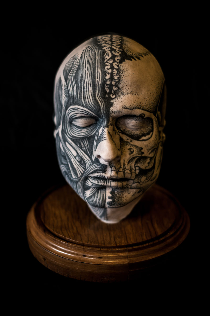 Tattooed sculpture head with intricate designs, showcasing tattoo culture creativity on a wooden base.