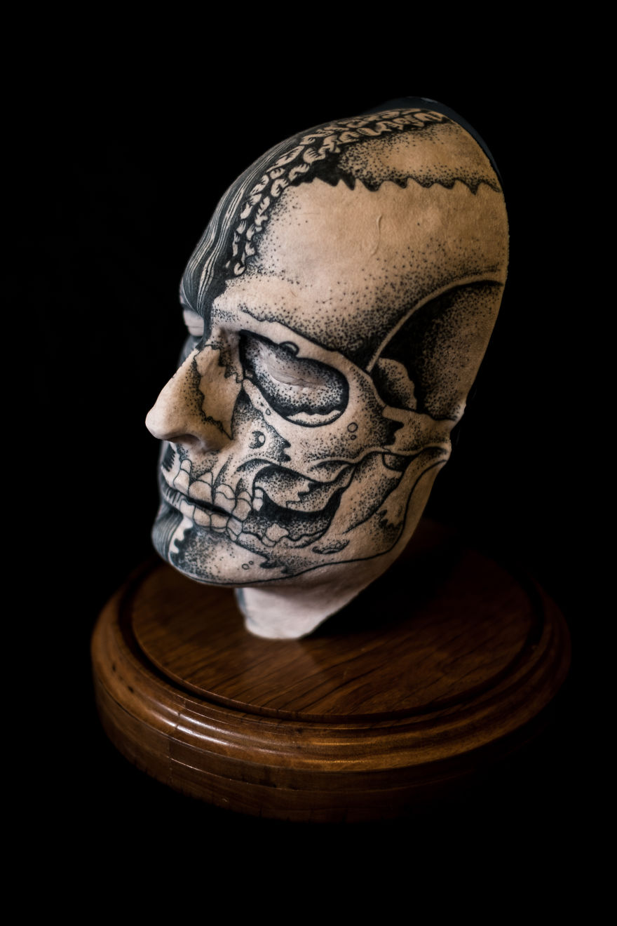 Tattoo culture: intricately tattooed skull sculpture displayed on a wooden base, showcasing creative artistry.