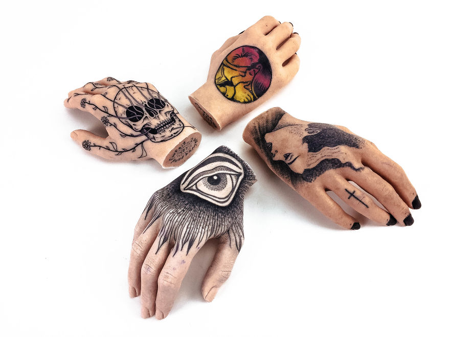 Tattoo culture art on sculpted hands, featuring detailed ink designs like skull, eye, face, and abstract.