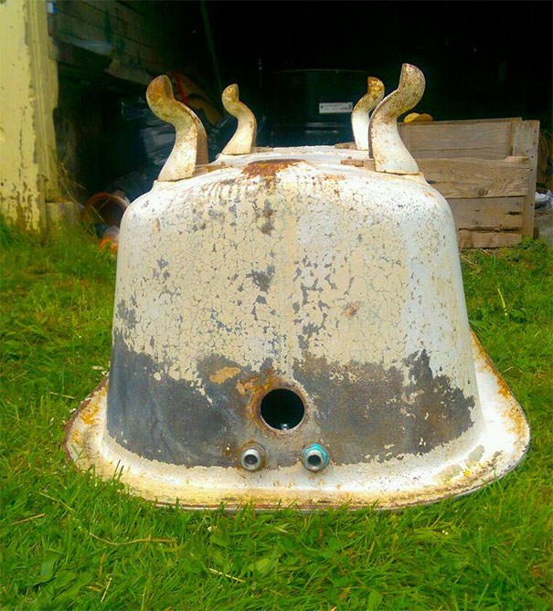Rusty metal object on grass resembling a face, a funny example of pareidolia in everyday objects.
