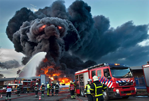Black smoke from a fire resembling a face with glowing eyes as firefighters and fire trucks respond at the scene, illustrating pareidolia.