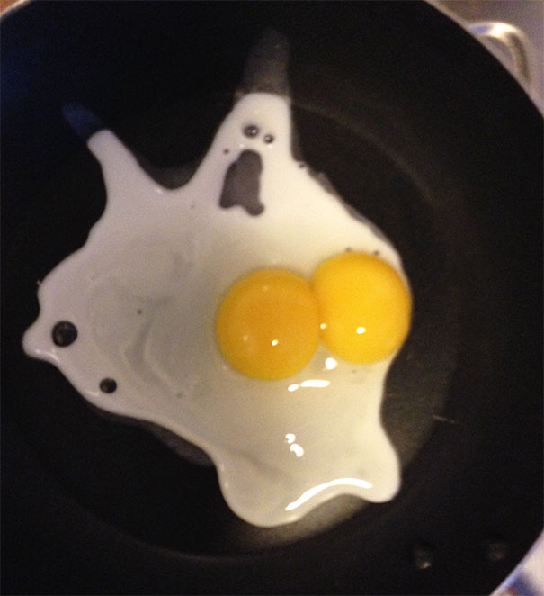 Fried egg in a pan resembling a ghost figure with two yolks and white forming a face shape, example of pareidolia.
