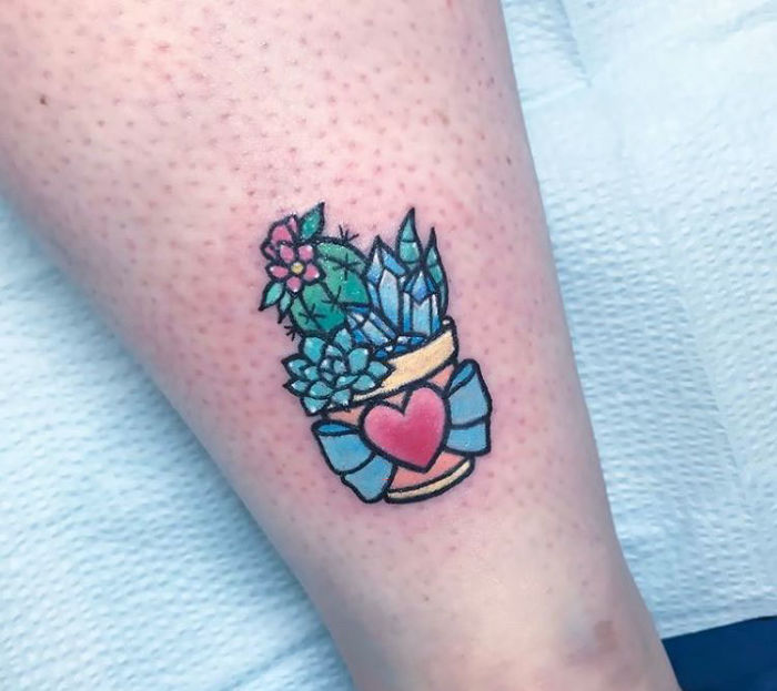 Colorful succulent tattoo on a leg featuring cacti, a heart, and a decorative pot.