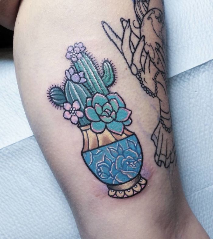 Colorful succulent tattoo in a vase on forearm, featuring cacti and flowers.