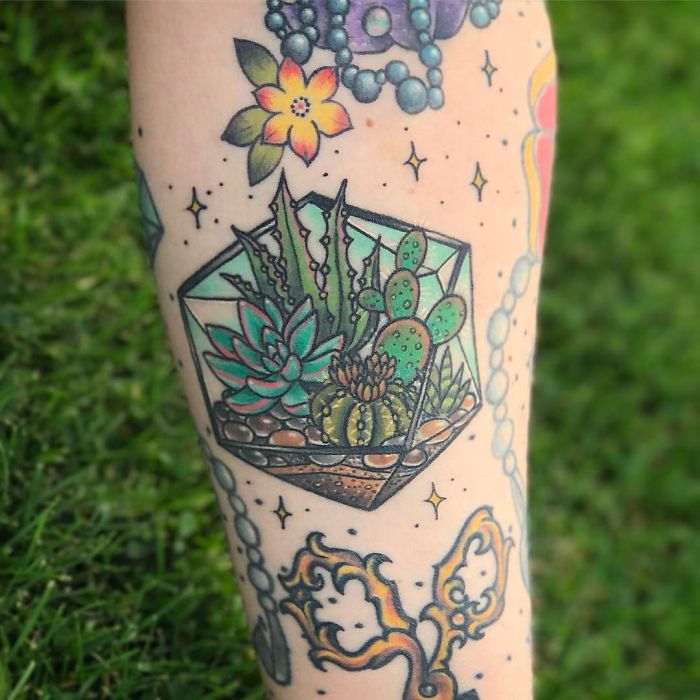 Colorful succulent tattoo on arm featuring various cactus and plant designs.