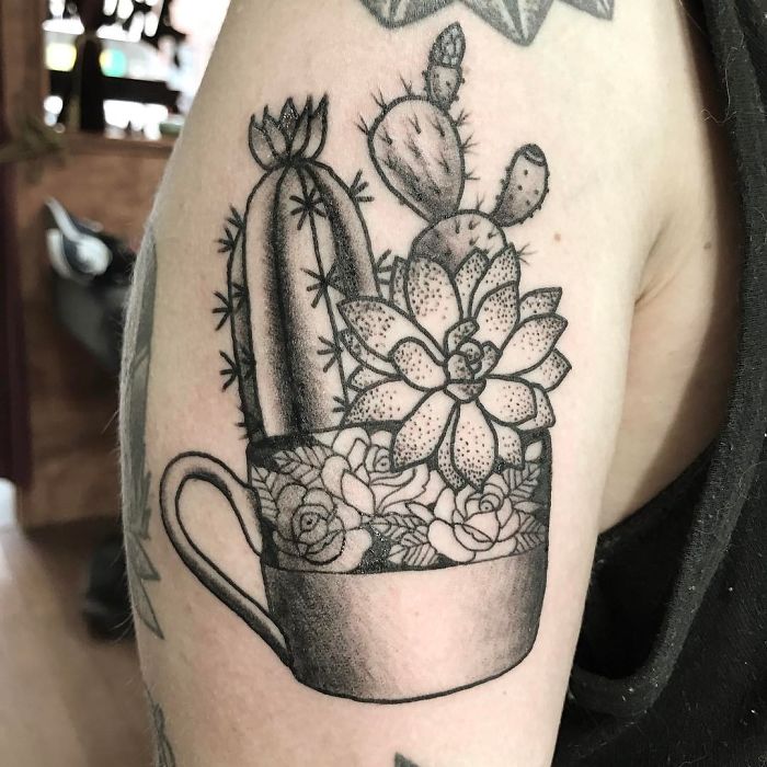 Black and gray succulent tattoo featuring various cacti inside a teacup on upper arm.