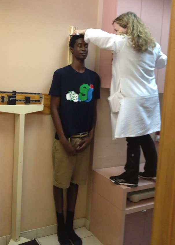 A tall person being measured for height by a woman standing on a raised platform, highlighting everyday struggles of tall people.