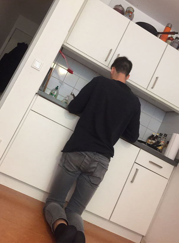 Tall person kneeling to use a low kitchen sink, illustrating everyday struggles of tall people in small spaces.