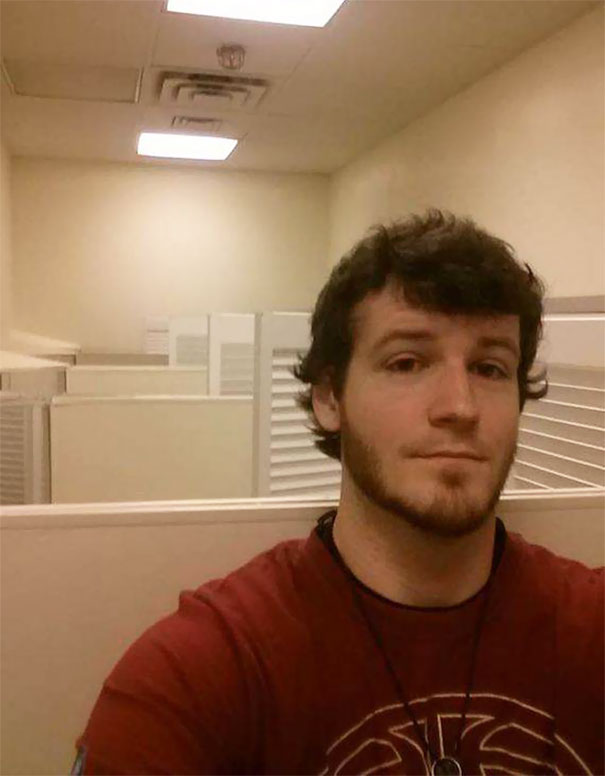 Young tall man taking a selfie in a small office cubicle, highlighting everyday struggles of tall people in tight spaces.