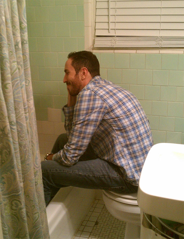 Man struggling to fit in small bathroom, highlighting everyday struggles of tall people in a cramped space.