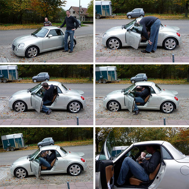 Tall man struggling to fit and sit inside a small silver car, illustrating everyday struggles of tall people.