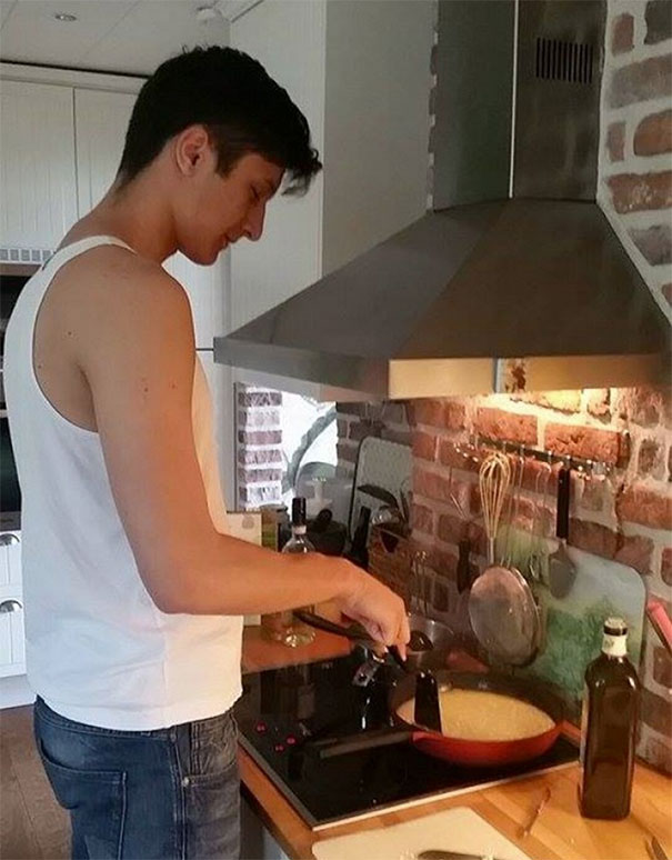 Tall man cooking in kitchen with a low stove hood, illustrating everyday struggles of tall people in funny situations.