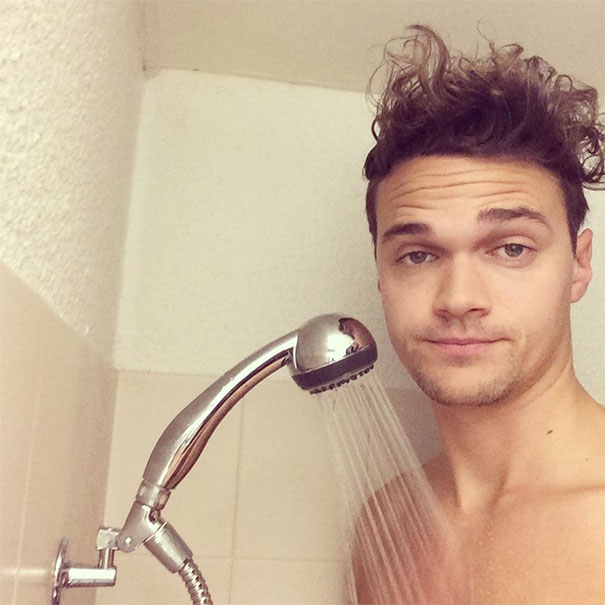 Young tall man with curly hair shows a low showerhead height, highlighting everyday struggles of tall people.