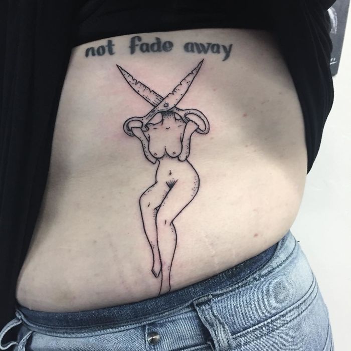 Tattoo of a headless girl on a person's side, featuring scissors and the phrase "not fade away."
