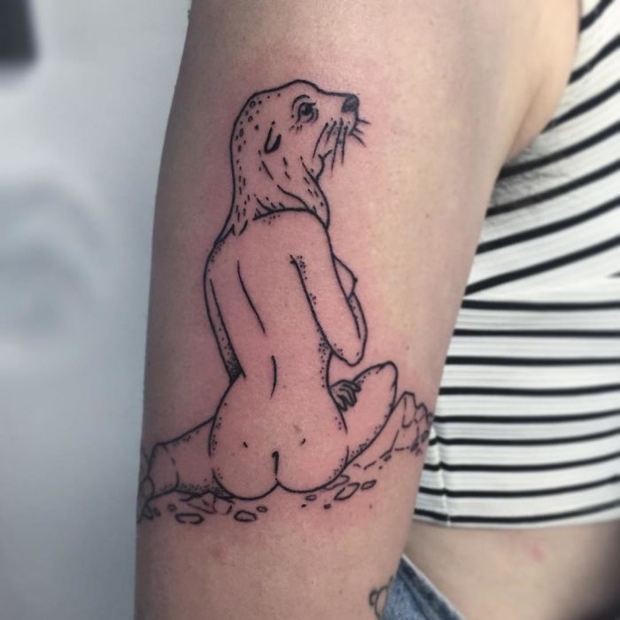 Tattoo of a headless girl with an otter's head on an arm, featuring stripes in the background.