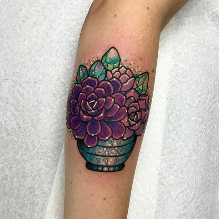 Colorful succulent tattoo on arm featuring vibrant purple and green hues in a decorative pot.