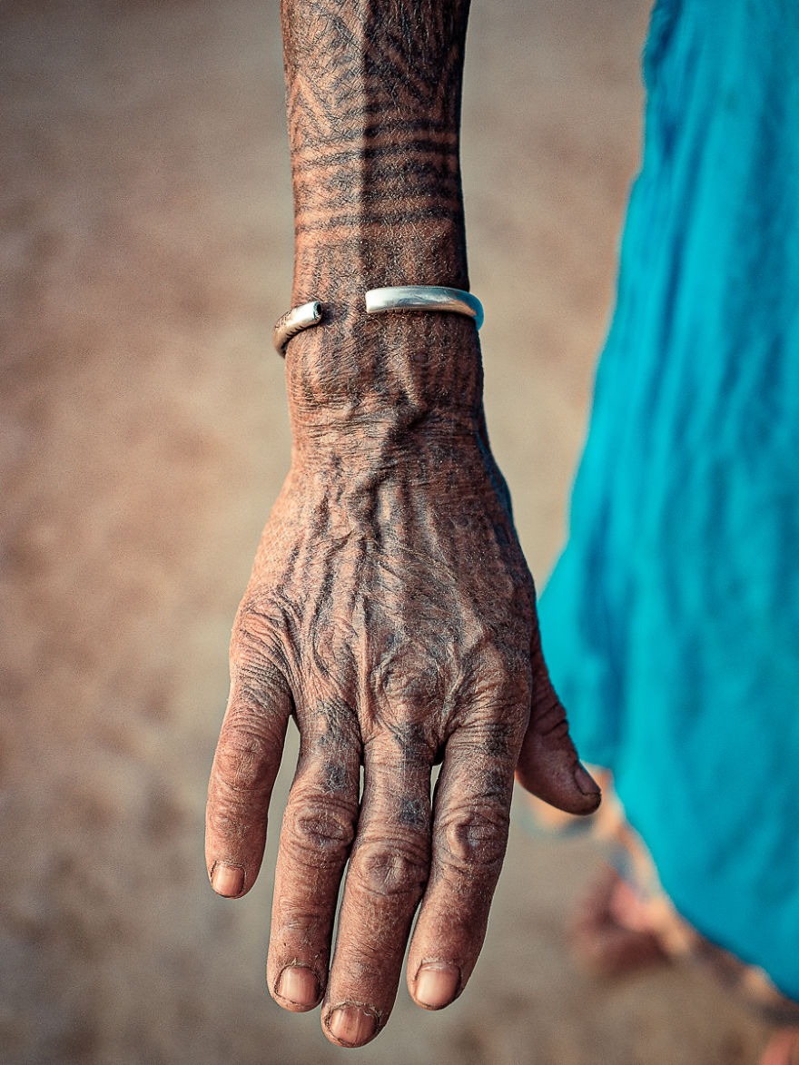 Tattooed hand of a Tharu tribe woman, showcasing intricate patterns and traditional jewelry.
