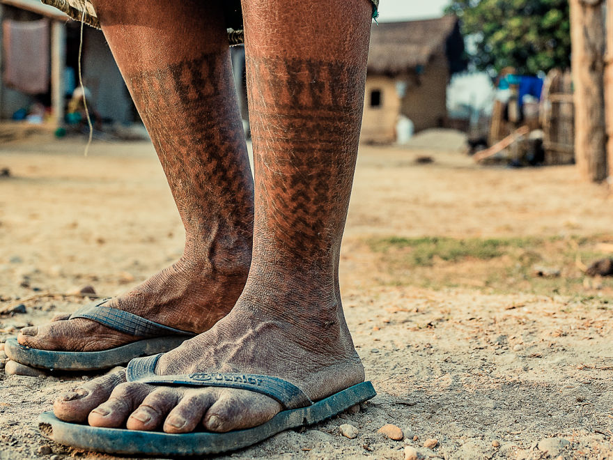 Tattooed legs of Tharu tribe woman in sandals on a dirt path, showcasing traditional tribal tattoos.