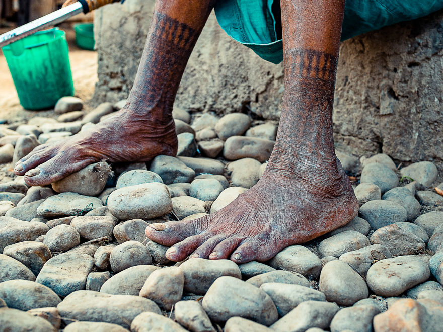 Tattooed feet of a Tharu tribe woman on pebbled ground, illustrating traditional body art.