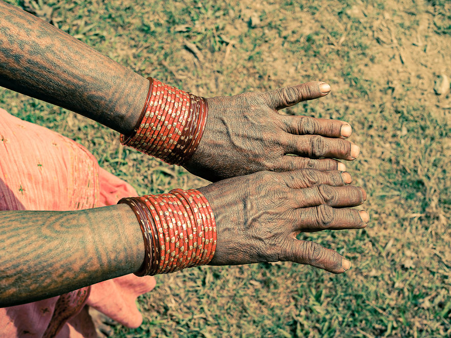 Tattooed hands of Tharu women with red bangles, showcasing tribal heritage and traditional art.