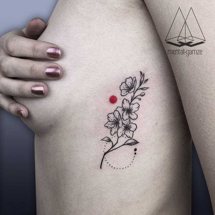 Floral tattoo with a red dot on skin, hand with pink nails gently touching the side.