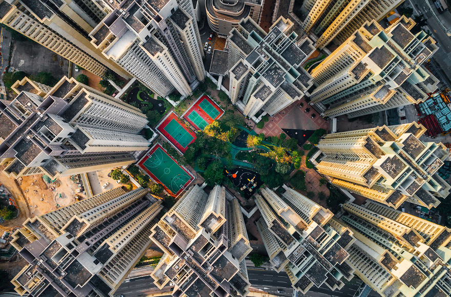 Aerial view of claustrophobic living spaces in Hong Kong with tall residential buildings surrounding small parks and courts.