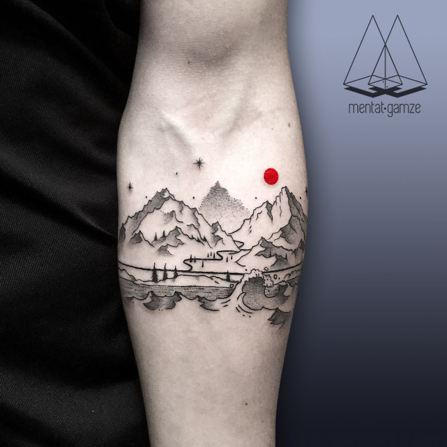 Tattoo artist's intricate mountain and ocean tattoo with a red dot on an inner arm.