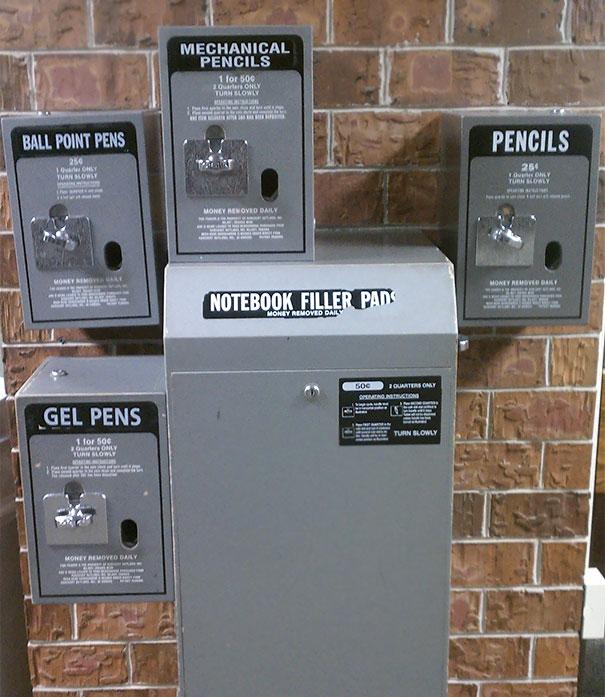 Vending machine for school supplies like pencils and pens against a brick wall.
