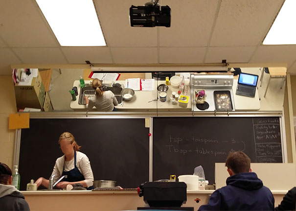 Cooking class demonstration with a teacher in front of a blackboard, viewed through a reflective mirror, showcasing genius school ideas.