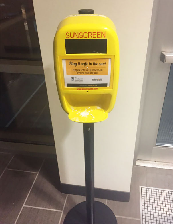 Yellow sunscreen dispenser in a school hallway for safety.