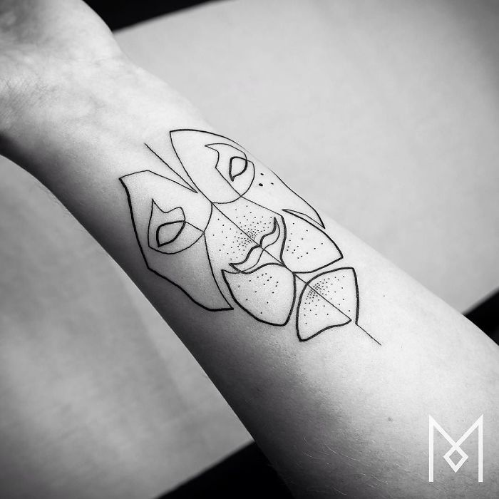 Single continuous line tattoo by Mo Ganji depicting a geometric face on a forearm.