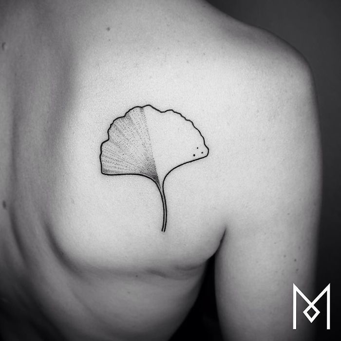 Minimalistic single-line tattoo of a leaf on a person's upper back by Mo Ganji.
