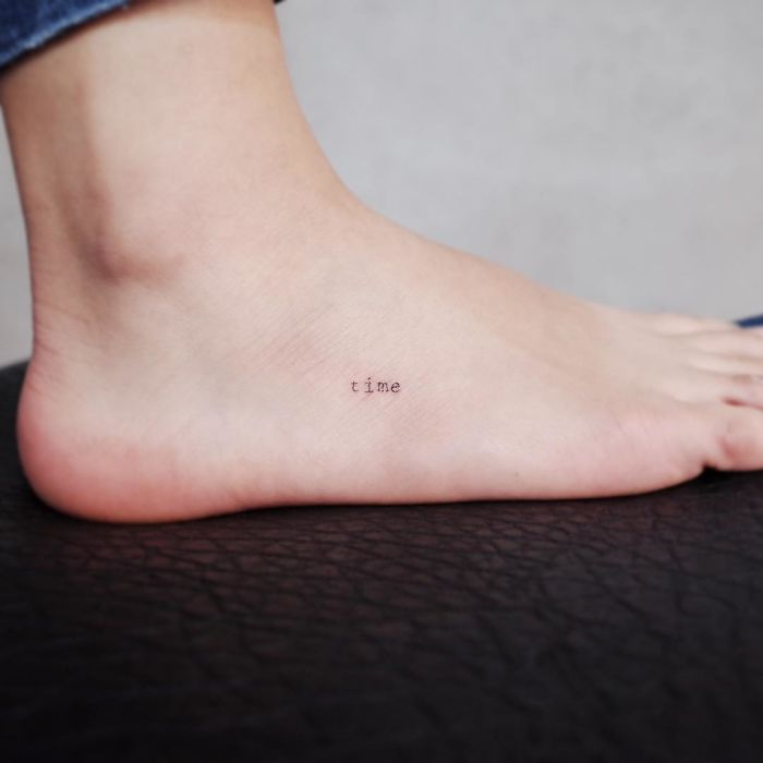 Minimalist tattoo of the word "time" on a person's foot.