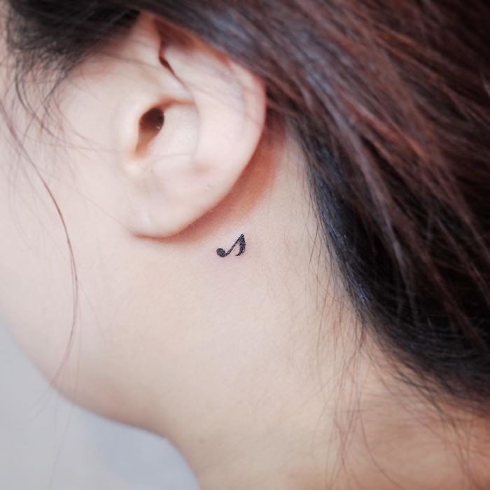 Minimalist music note tattoo behind the ear.
