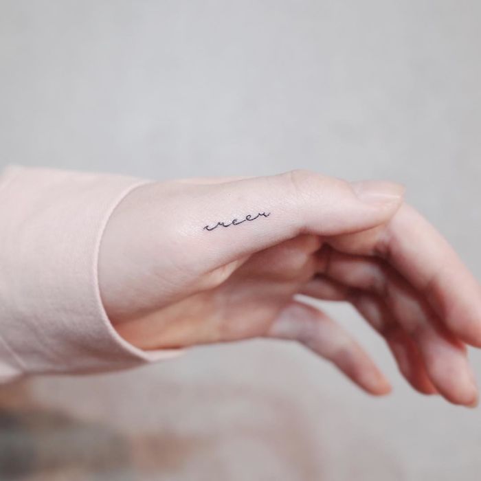Minimalist tiny tattoo on a person's hand in cursive script, embodying discreet tattoo art.